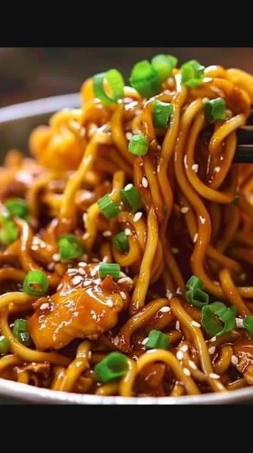 Delicious sticky garlic chicken noodles served in a bowl garnished with green onions.